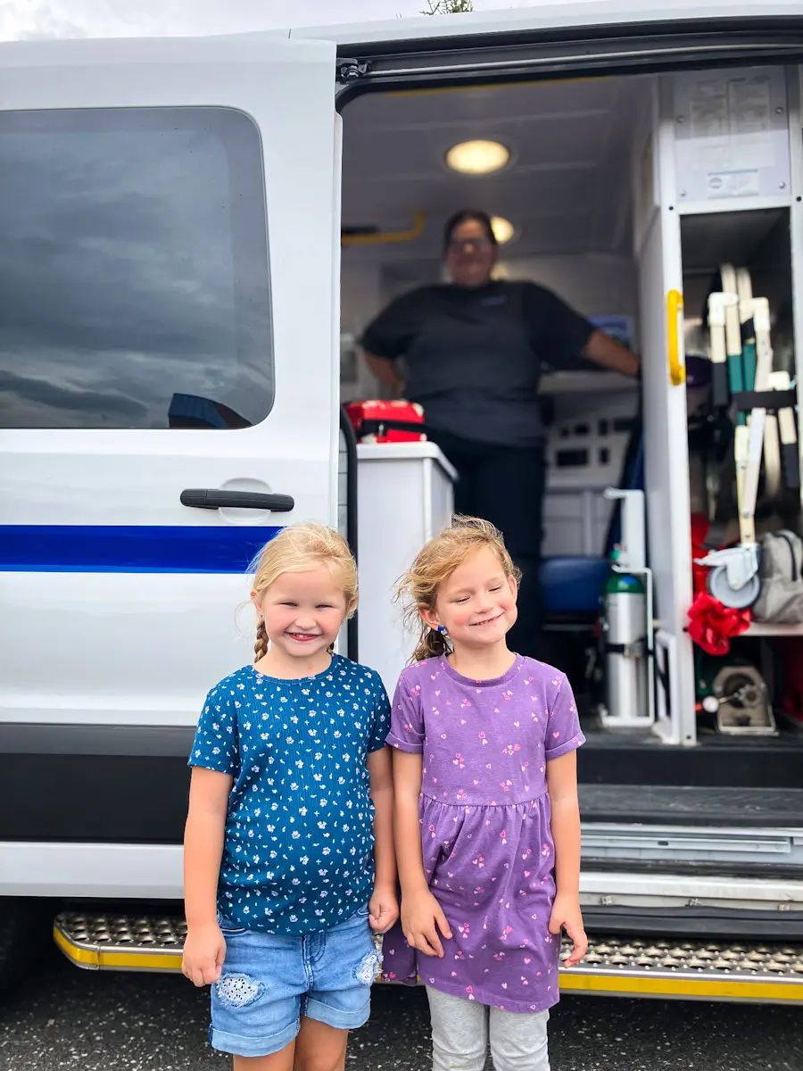 Two children standing in front of an ambulance with an EMT in the background