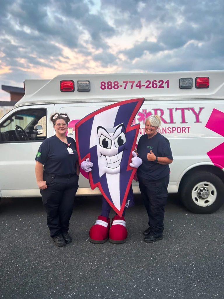 Two EMTs posing with a mascot in front of an ambulance